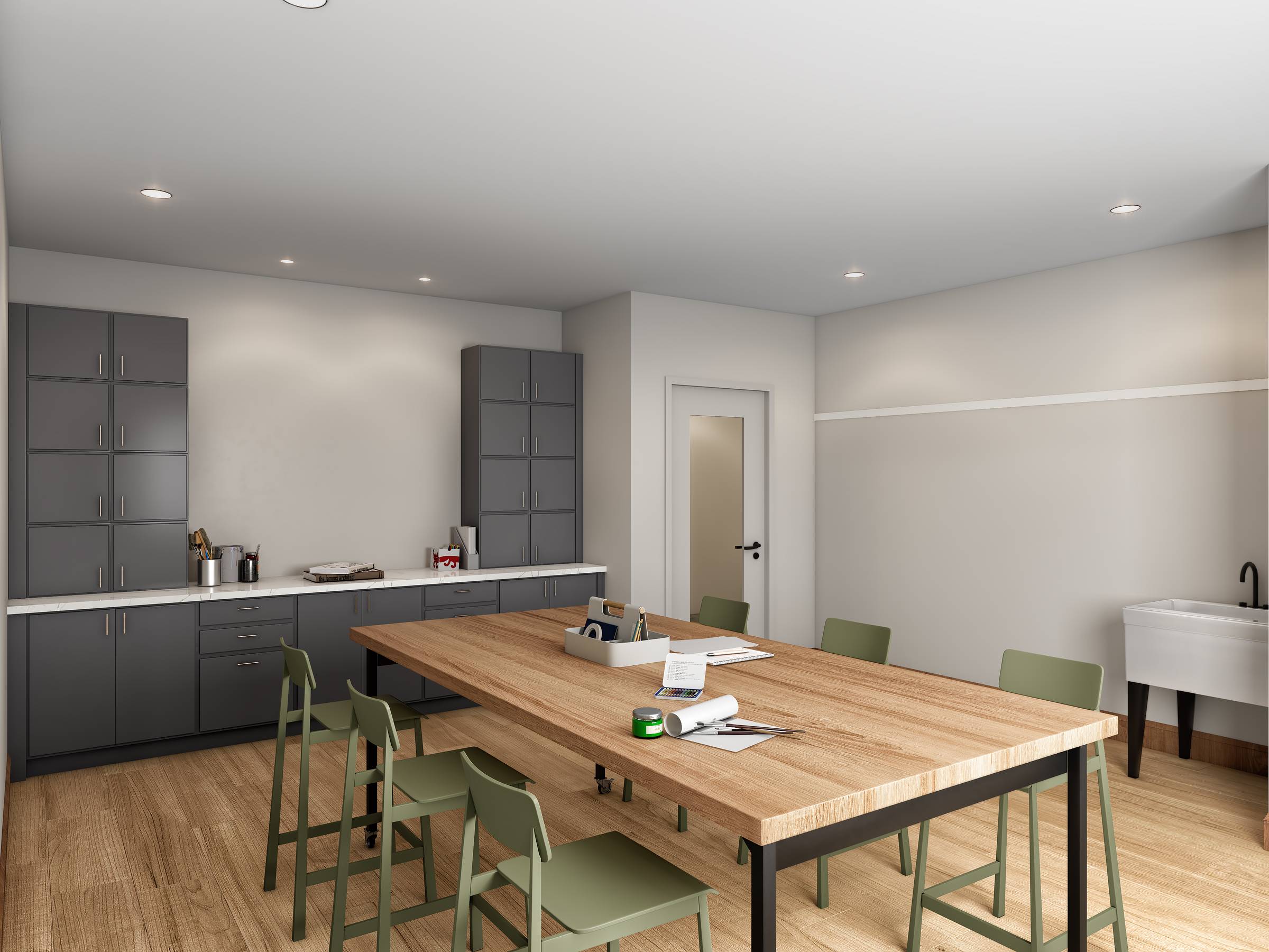 A modern break room with gray cabinets, a large wooden table, green chairs, and scattered papers and mugs.