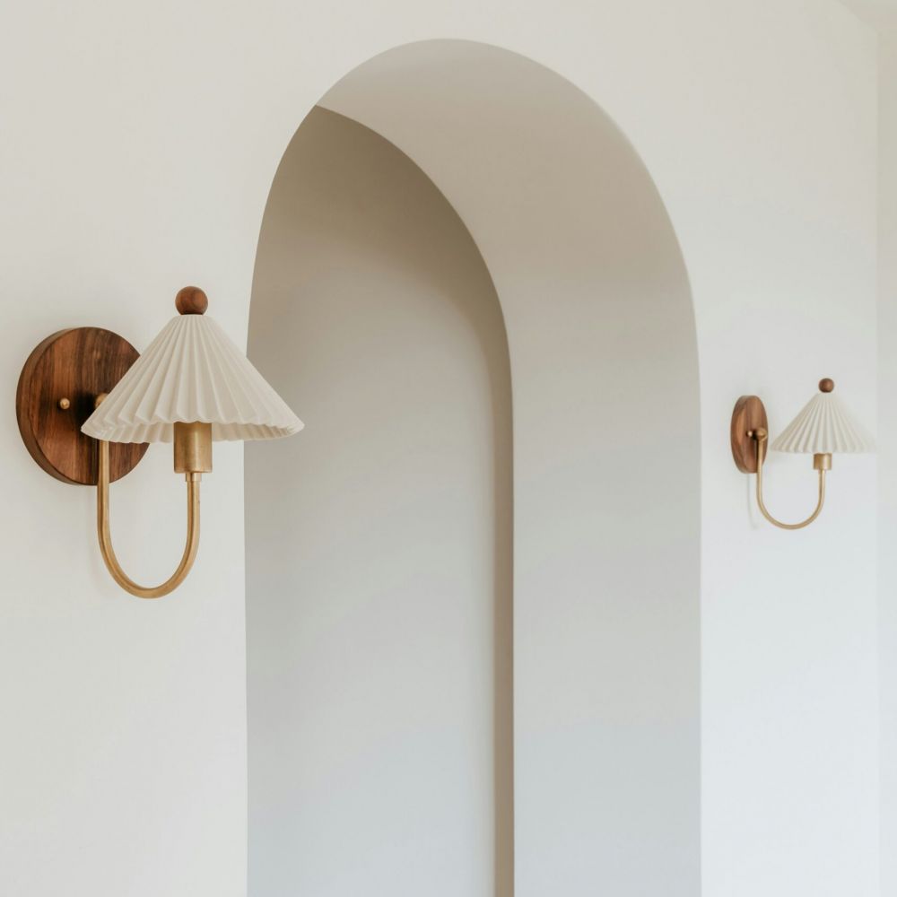 Minimalist wall lamps with pleated shades flank a white, arched doorway in a modern interior.